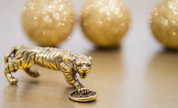 A bronze figure of a tiger with a coin - the symbol of the Chinese new year 2022 on a background of golden glitter balls, a copy space. Wishes of good luck, financial well-being and wealth.
