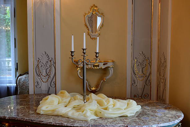 A close up on an old, decorative candlestick standing next to velvet cloth, a mirror and a shelf situated near a highly decorated wall of a historic manor seen on a cloudy autumn day in Poland